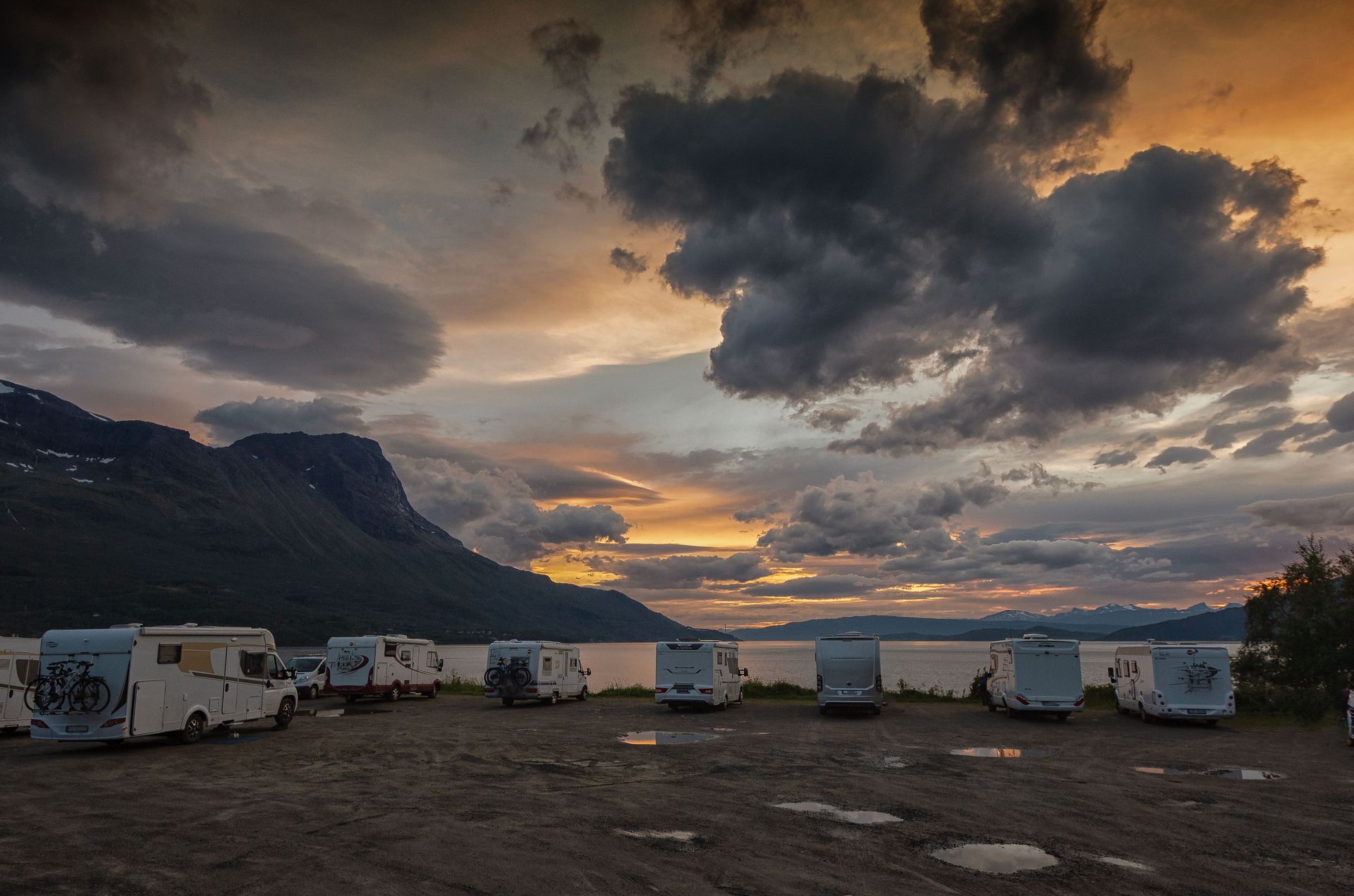 Stunning sunset view over a scenic Norwegian campsite with parked RVs and dramatic clouds.