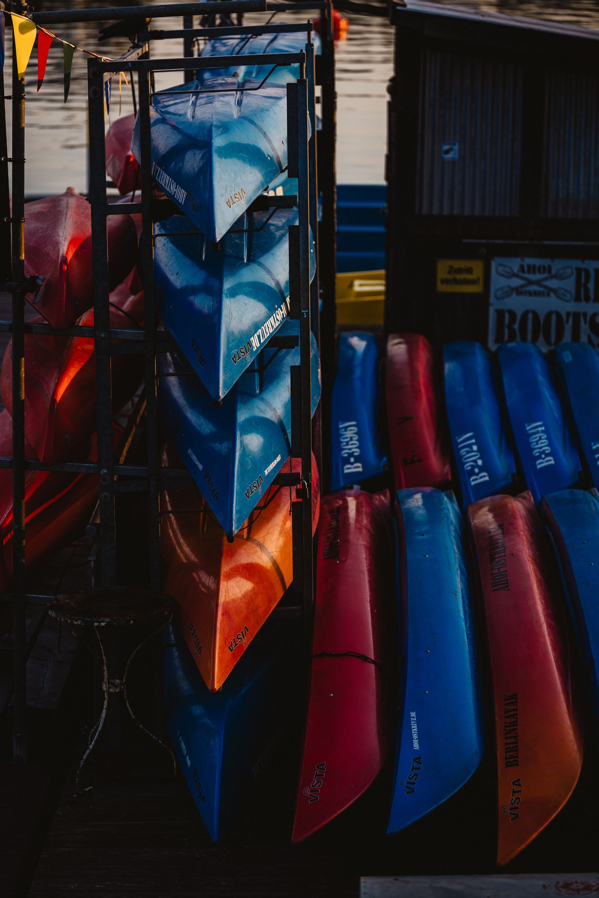 Colorful kayaks stacked at a serene waterfront during daylight.